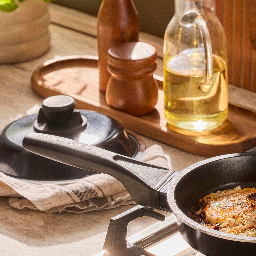 Black cast iron cookware on a wooden surface with a bottle of oil and wooden containers.