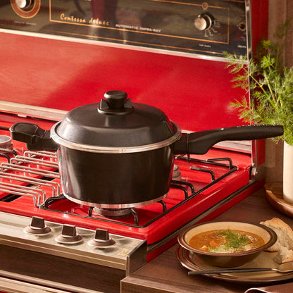 Black pot on a red stove with a bowl of soup on a wooden table