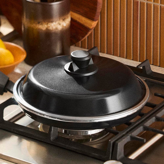 Black pot lid on a gas stove with a wooden wall in the background