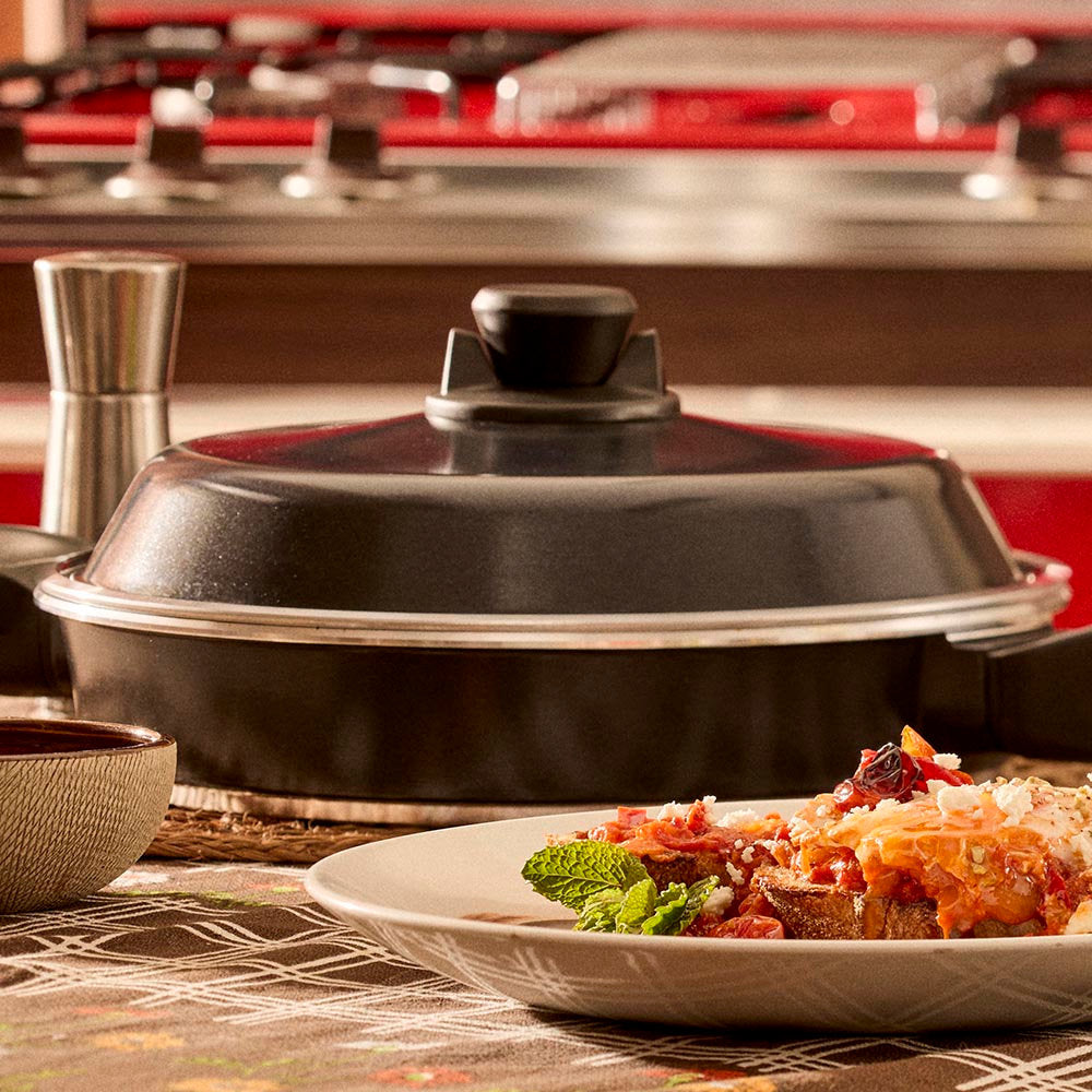 Black covered dish on a kitchen counter with a plate of food in the foreground