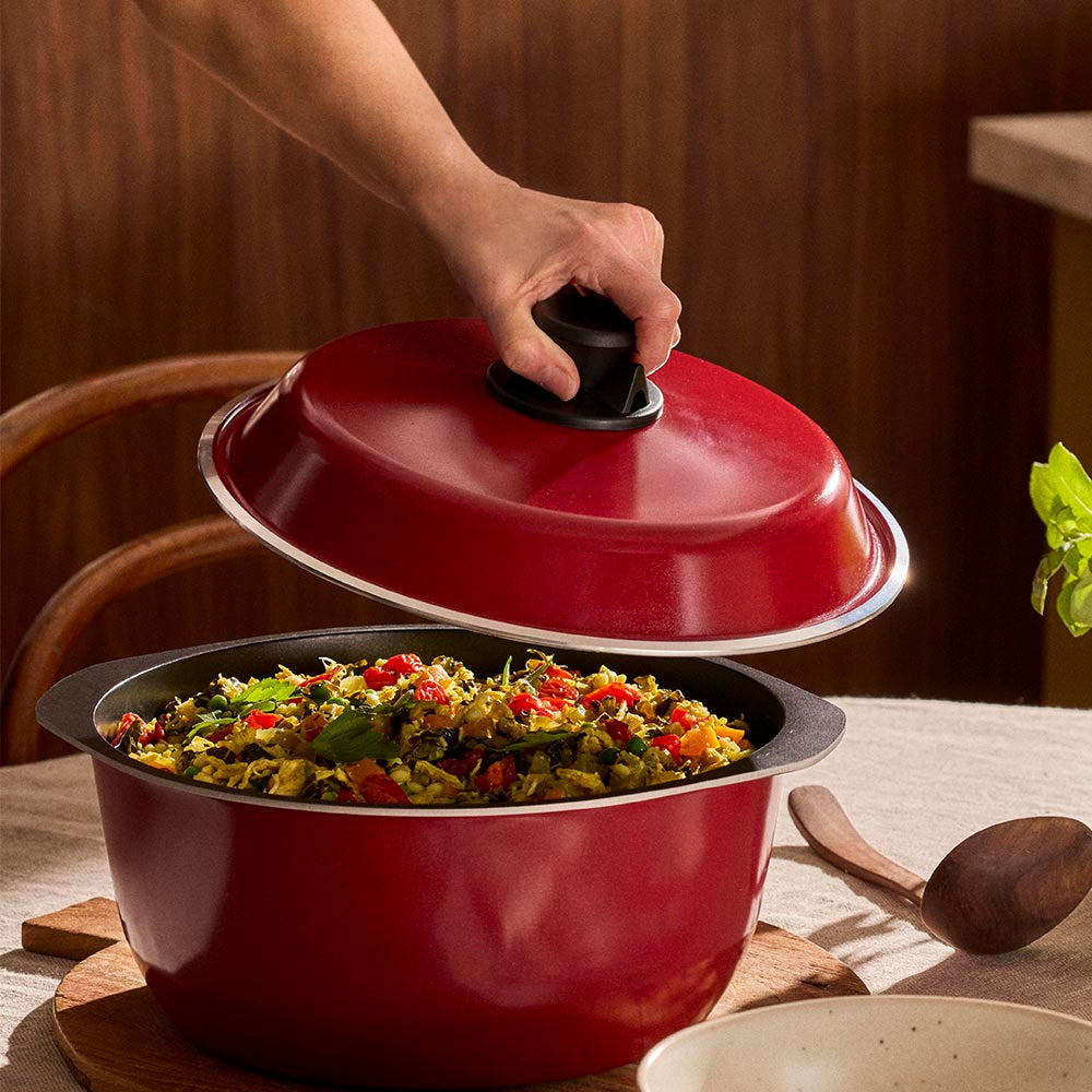 Red pot with a lid being lifted to reveal stir-fry on a wooden table.