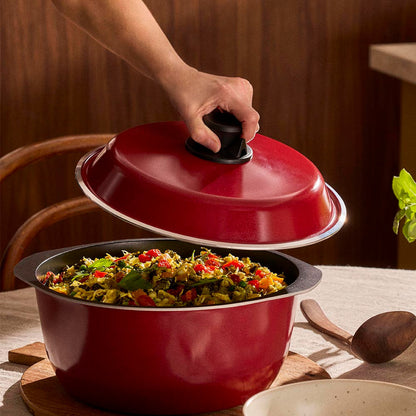Red pot with a lid being lifted to reveal stir-fry on a wooden table.
