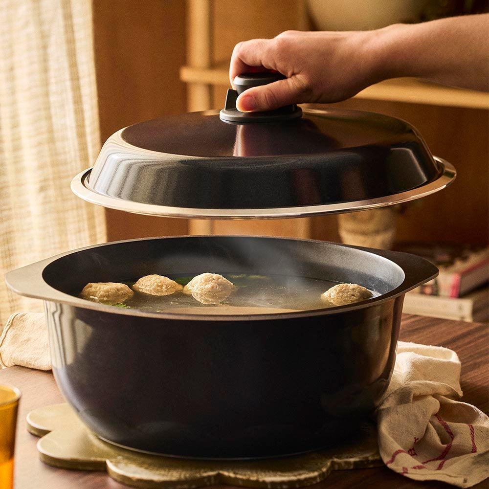 Person closing a black pot with a lid on a wooden table.