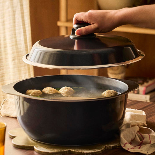 Person closing a black pot with a lid on a wooden table.