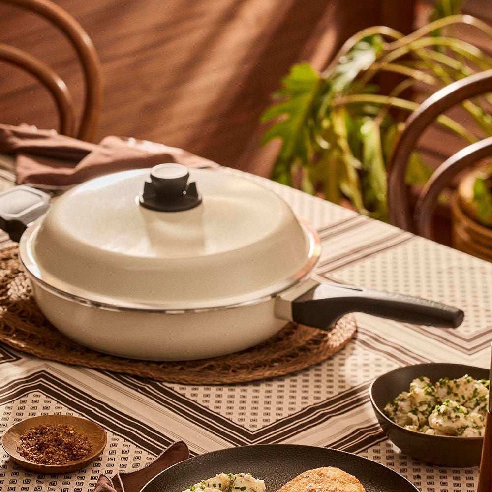 White frying pan with a lid on a table with food and decor