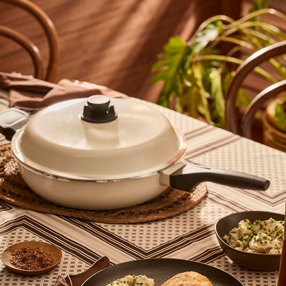 White frying pan with a lid on a table with food and decor