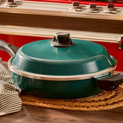 Teal frying pan with lid on a wooden surface in front of a stove.